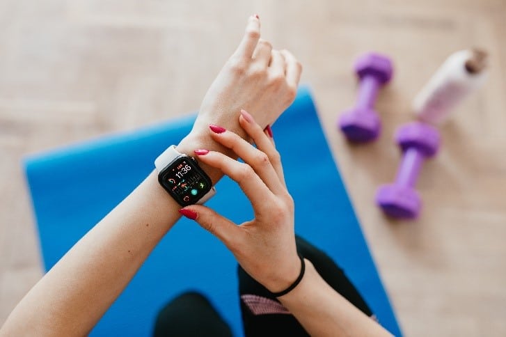 Woman looking at smart fitness tracker. Yoga mat and dumbells in the background