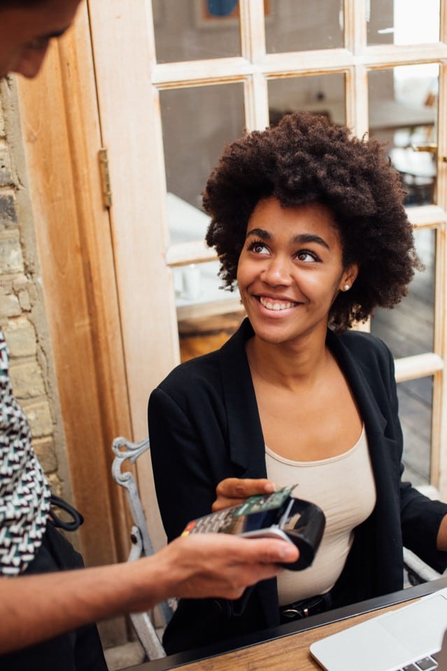 Businesswoman making payment via processing terminal whilst sat down in a restaurant 