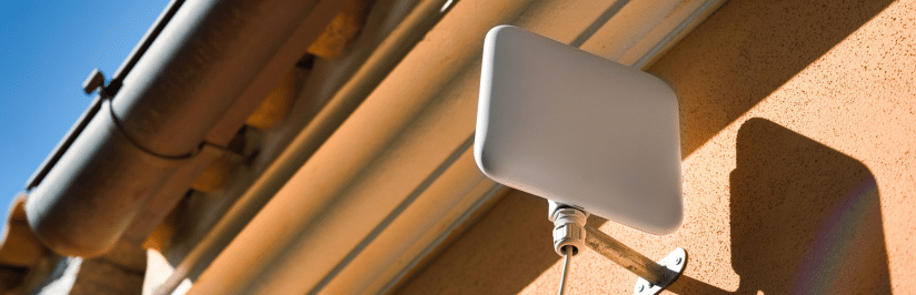 A rectangular external antenna for fixed wireless access (FWA) is mounted on the wall of a building, with a blue sky and part of a rain gutter visible in the background.