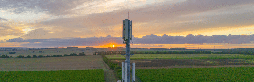 A cell tower stands in the center of green fields at sunrise, supporting 5G FWA technology beneath a colorful sky and clouds in the background.