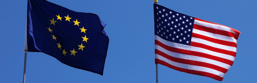 The European Union flag and the United States flag are flying on flagpoles against a clear blue sky.