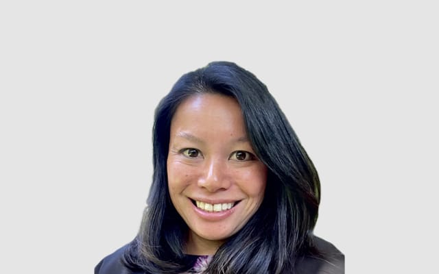 Woman with long dark hair smiles at the camera. She is wearing a dark top and is posed against a plain light background, representing one of the eseye board members.